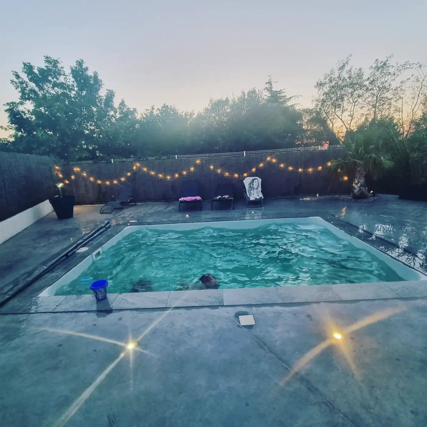 Piscine éclairée au crépuscule avec une guirlande lumineuse au-dessus de la plage